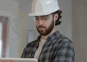 Propiedad Horizontal Male construction engineer assessing building plans indoors, wearing a hard hat.